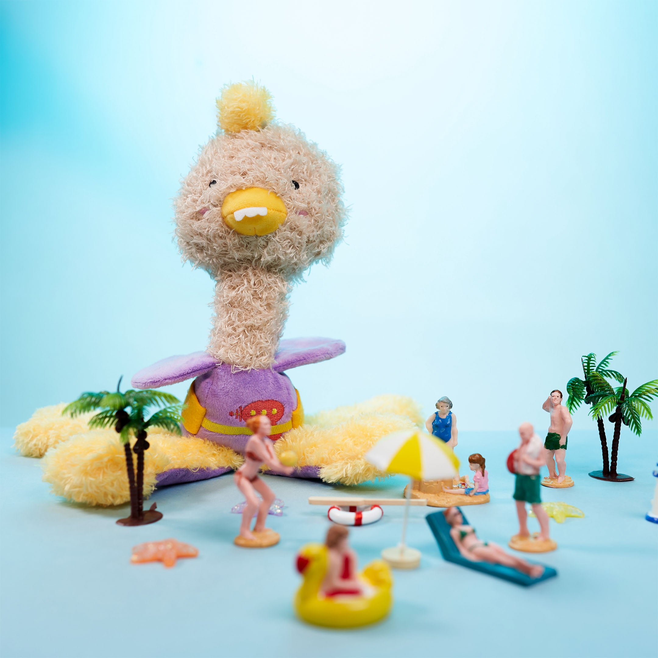 OstriKraken dog toy by The Furryfolks, a blend of an ostrich and Kraken, showcased in a beach-themed scene with miniature figures enjoying a sunny day. This interactive nosework toy includes a treat pocket to engage dogs in playful activity.