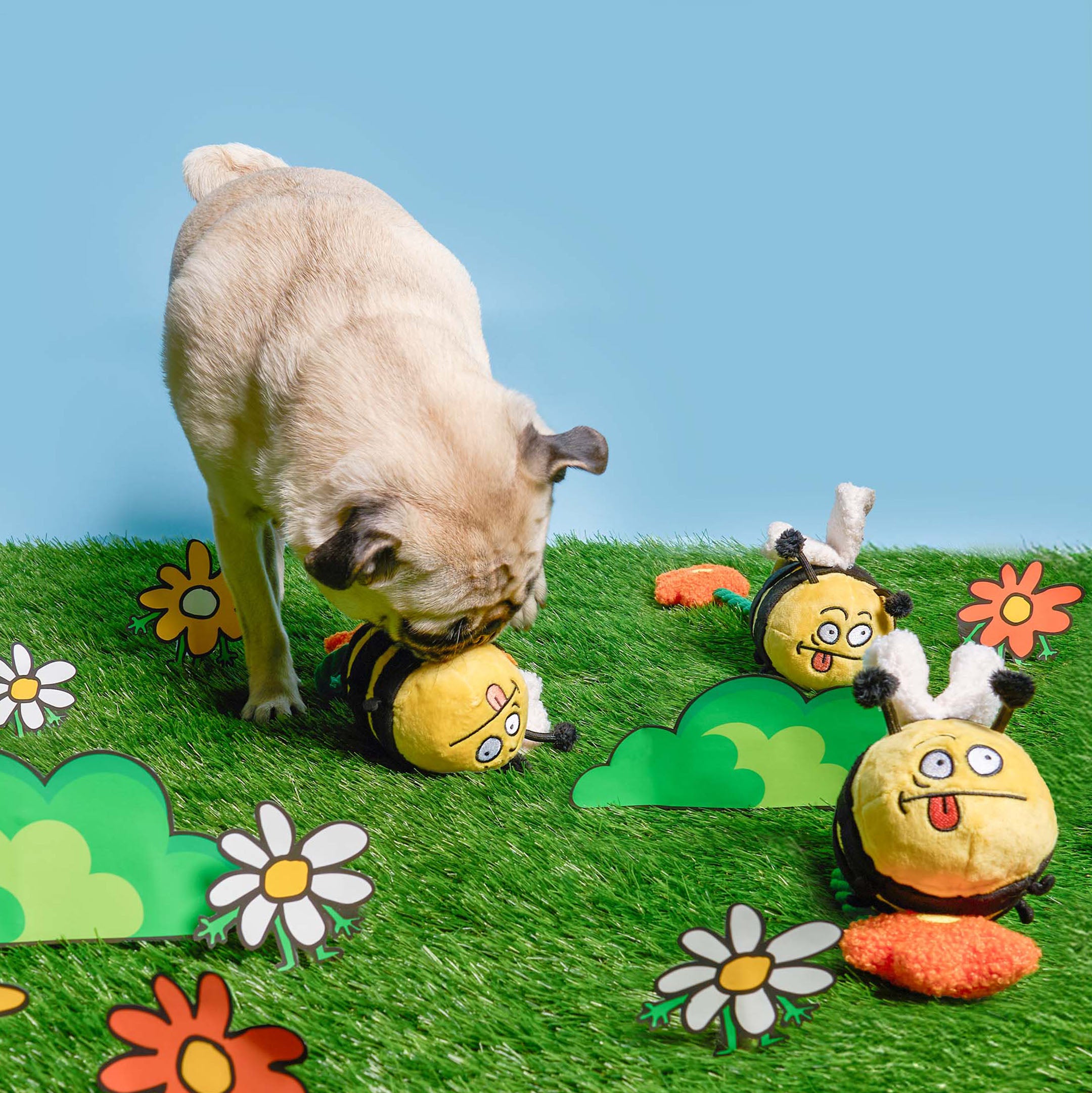 Dog playing with a bee-themed ball on a grassy area with cartoon bee and flower decorations.