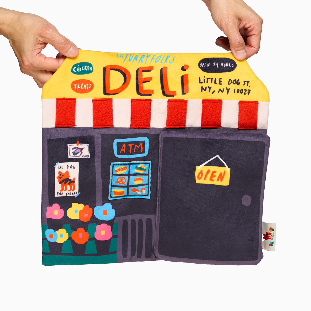 Deli storefront Nosework mat held open by two hands, featuring a yellow DELI sign, red-and-white striped awning, colorful flowers, and a purple door.
