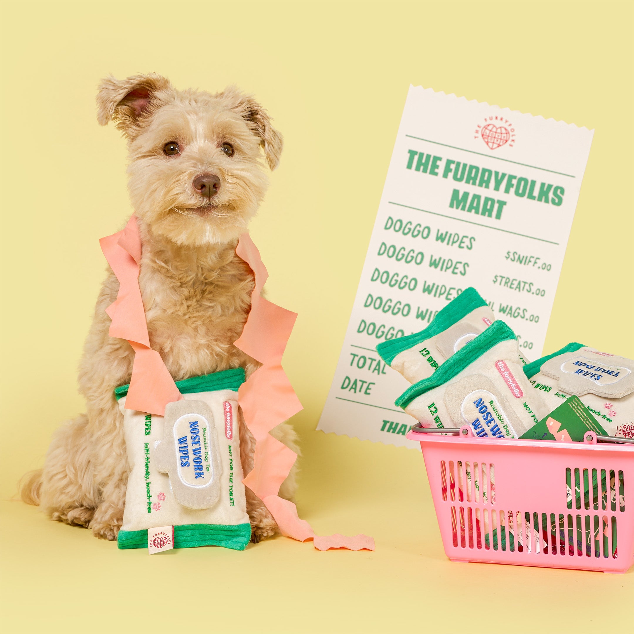 Dog wearing a pink outfit with doggy wipes and a shopping basket on a yellow background