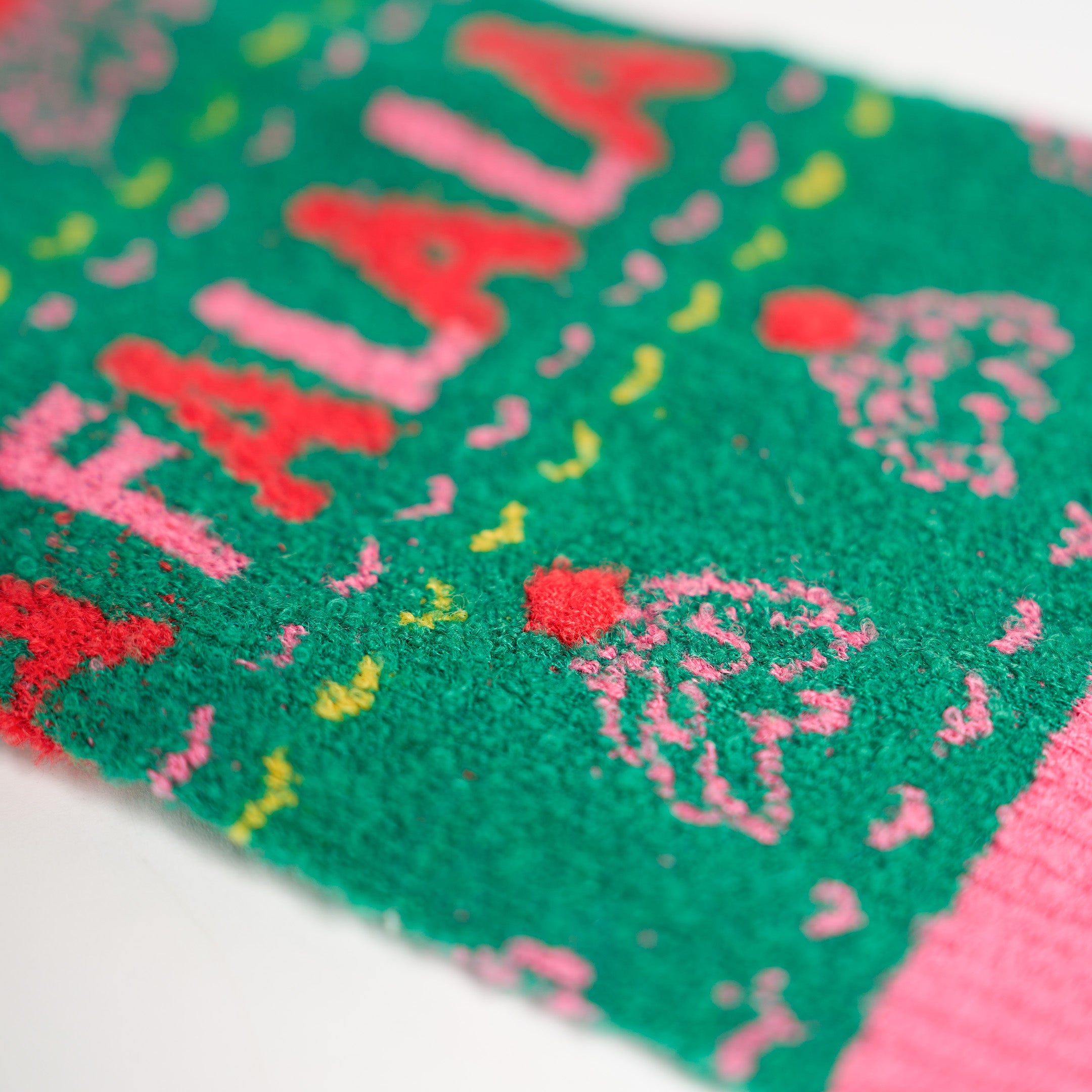 Close-up of a green sweater with pink text and patterns on a white background