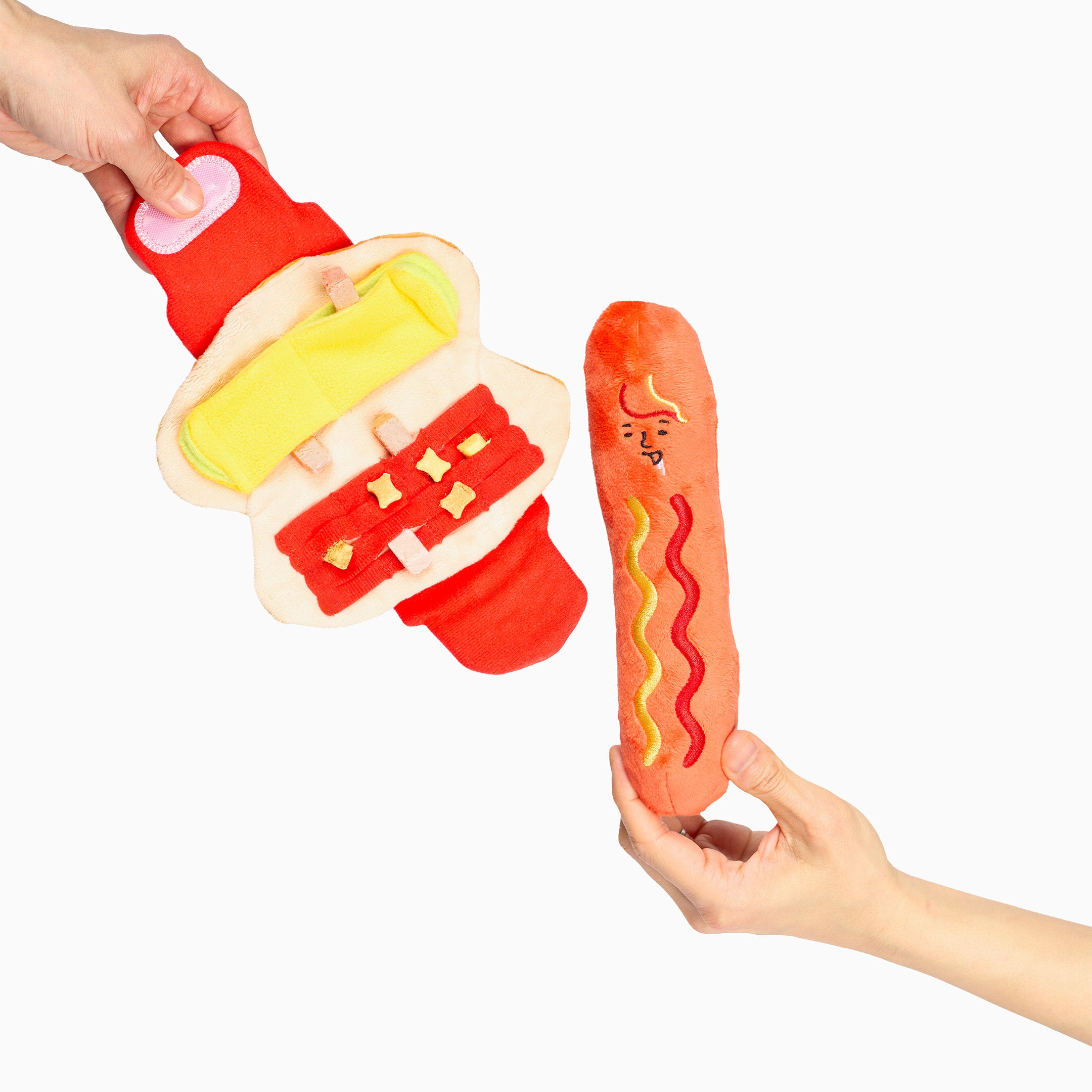 Plush toy resembling a hot dog with a bun held by hands on a white background