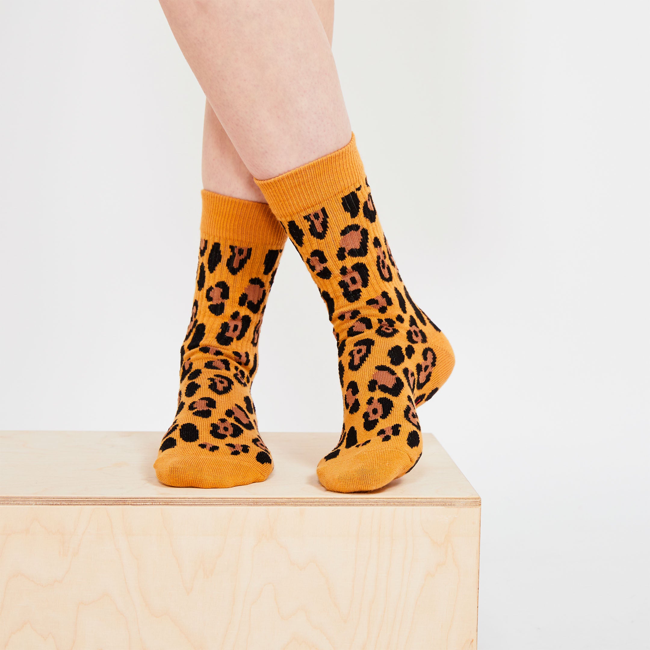 A close-up shot of crossed legs wearing leopard-print socks, placed on a light-colored wooden platform.