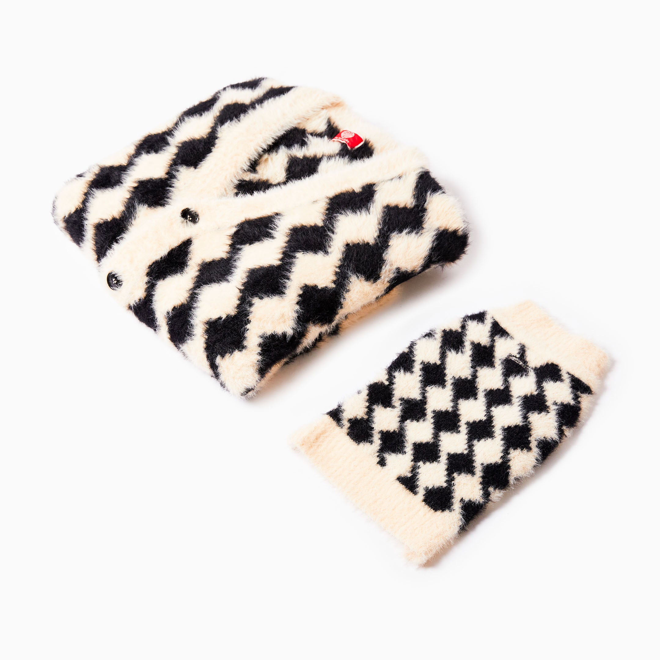 A folded black and cream-colored cardigan with a bold diamond pattern, placed next to a matching dog sweater, both showcasing their soft, fluffy material.