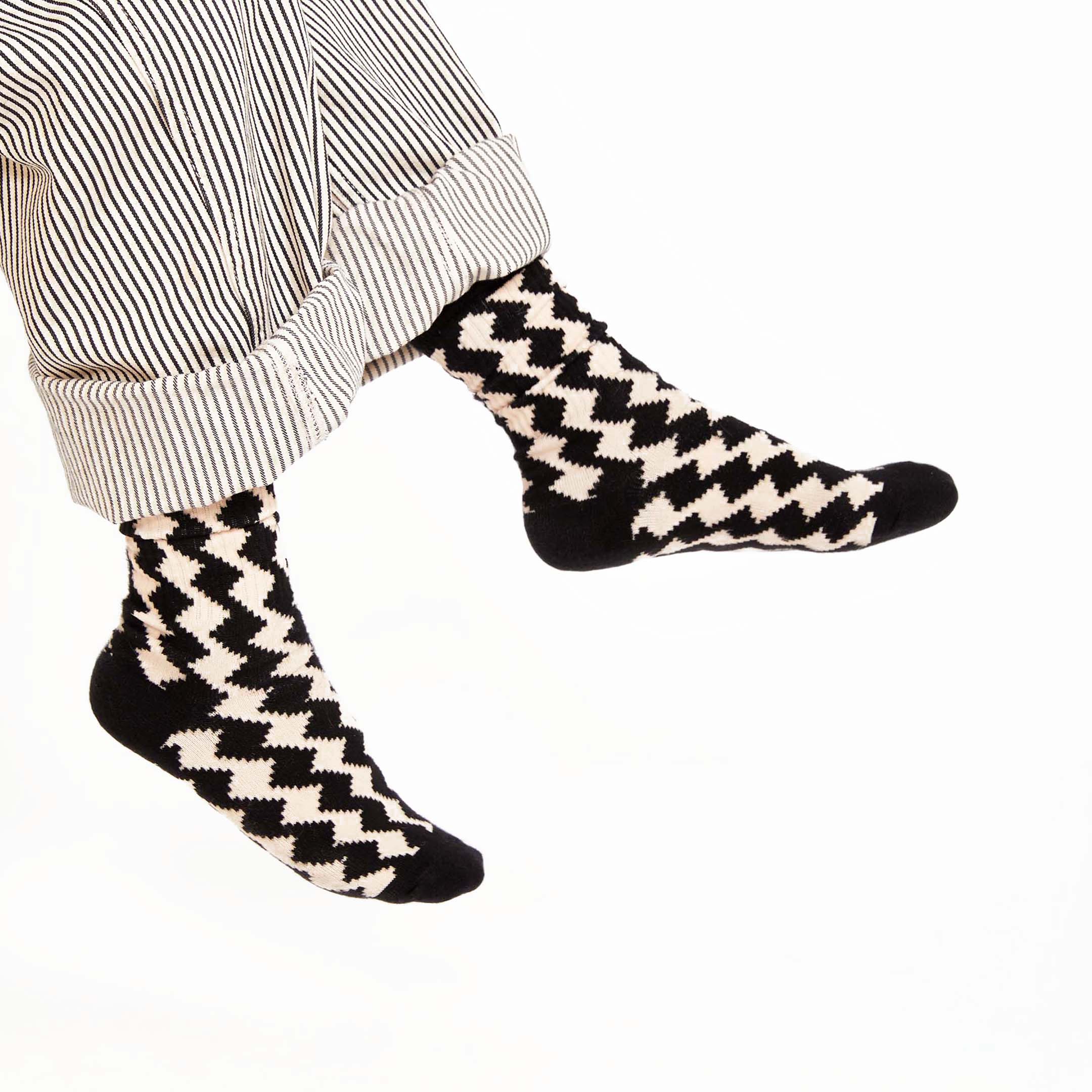 A stylish close-up featuring bold black-and-white socks with a striking pixelated diamond pattern. Paired with cuffed, striped pants, these socks add a modern and playful twist to any outfit!