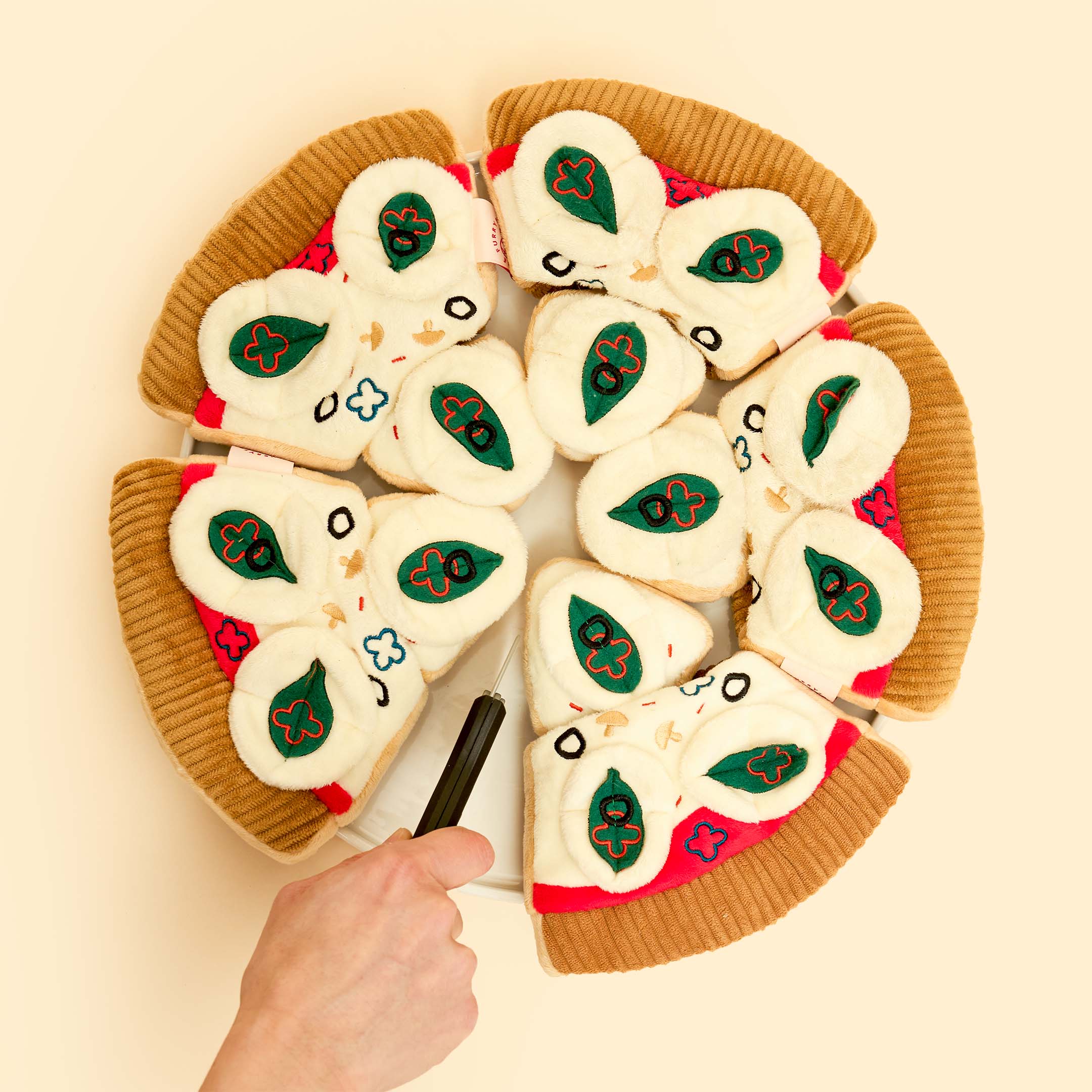 A full “pizza” made of plush pizza slice nosework toys arranged in a circle, with a hand playfully lifting a slice. A creative and fun presentation of the furryfolks’ interactive dog toy.