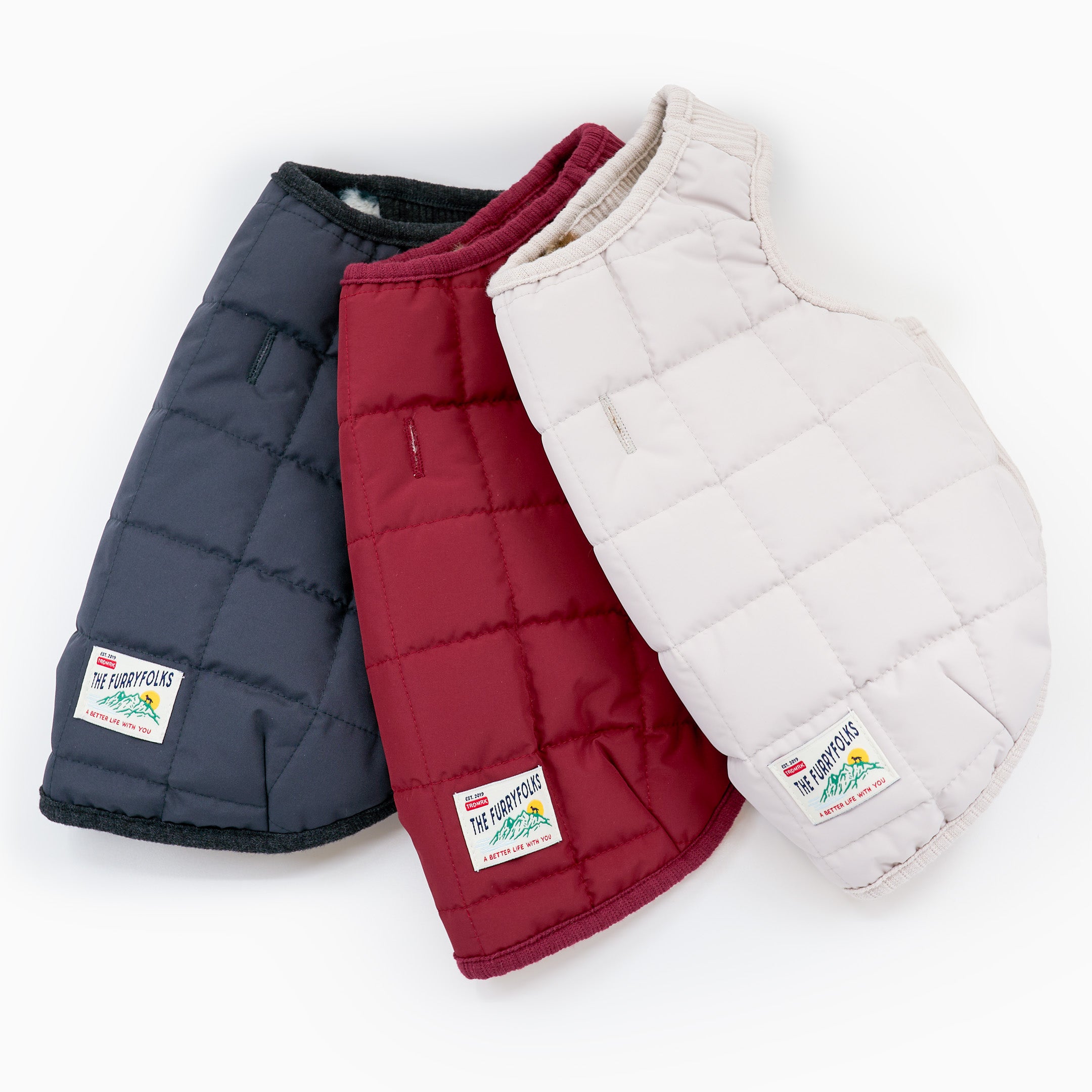 Three puffer vests in navy, red, and white on a white background