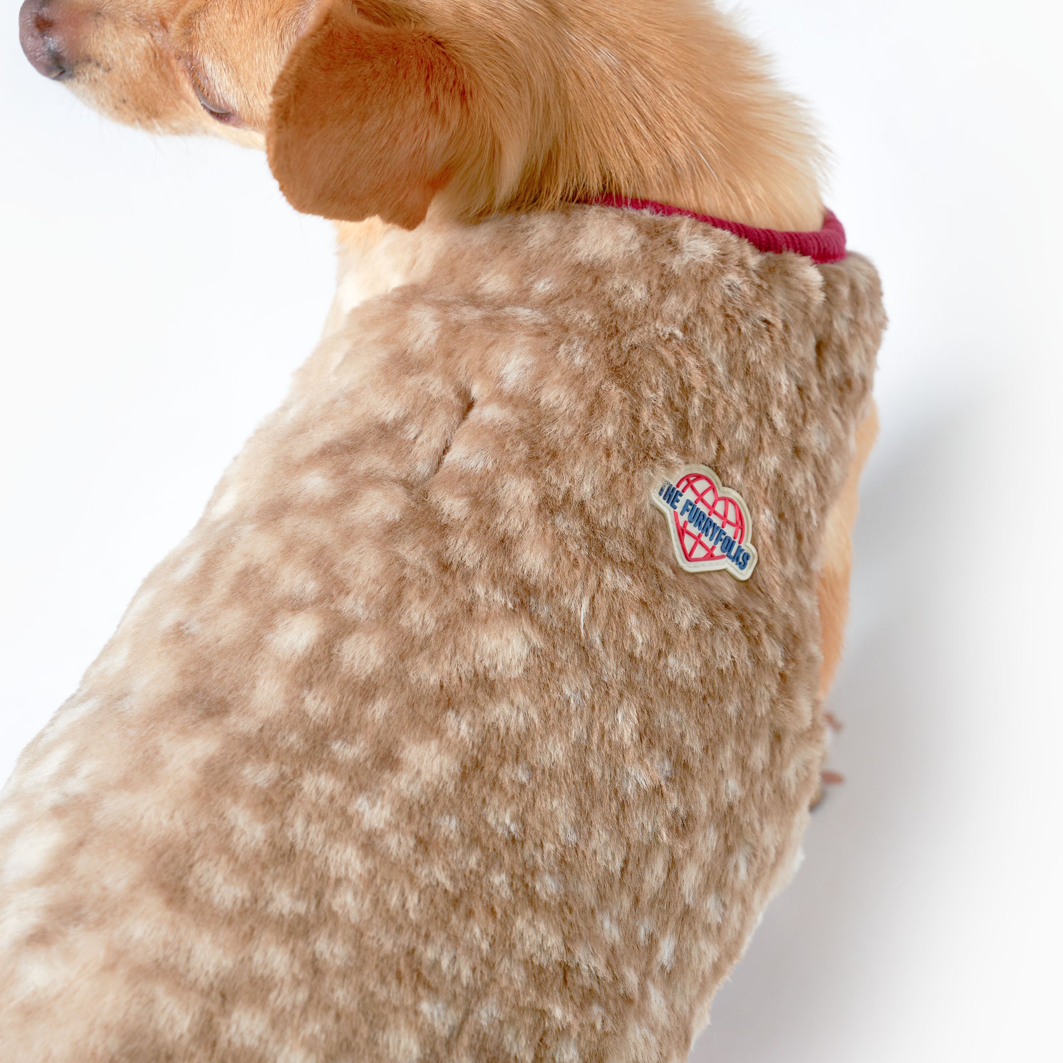 Dog wearing a beige fleece coat with a visible brand logo on a white background