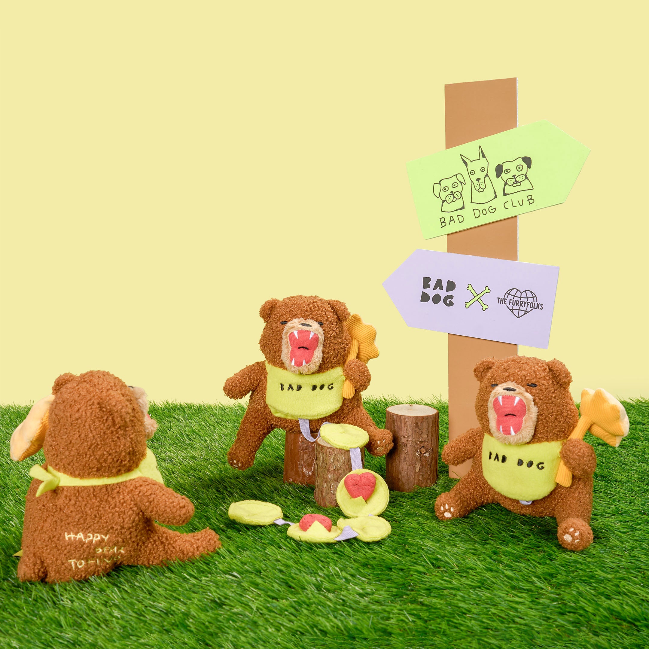 Three teddy bears with 'Bad Dog' signs in a grassy area with a wooden post and signs.