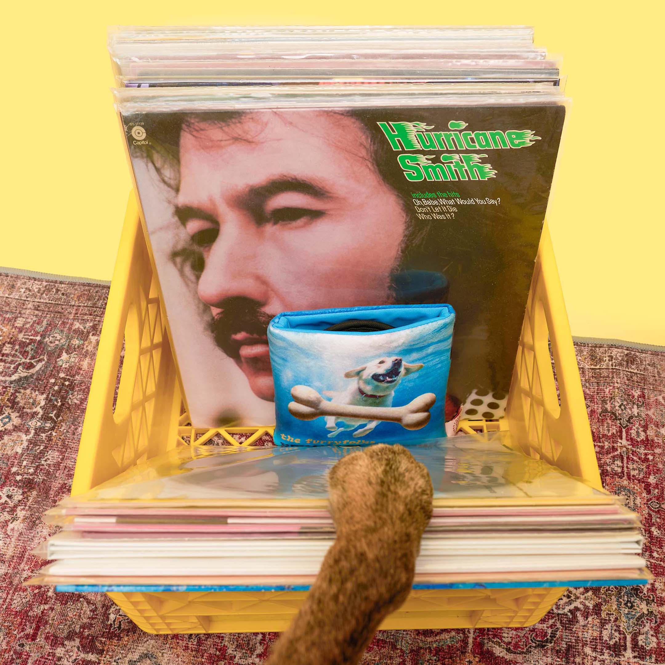 A dog’s paw reaches into a yellow record crate to pull out the furryfolks’ “Spin ‘N’ Sniff Vinyl” nosework toy, placed in front of a Hurricane Smith album.