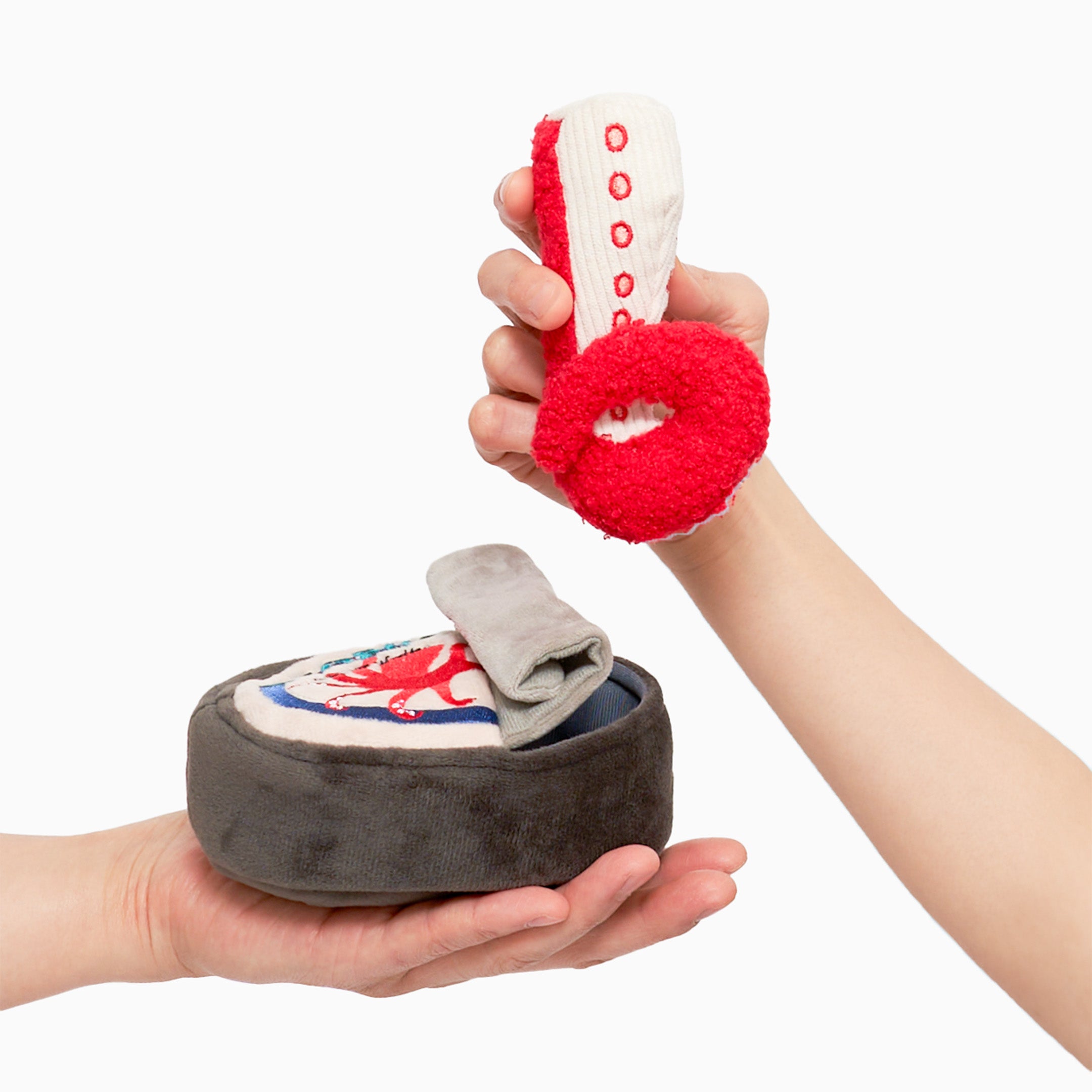 One hand is holding a plush toy shaped like a can of octopus, which is dark brown with a cream-colored label. The label features a red octopus illustration and the word “OCTOPUS” in blue letters. Another hand is lifting a red and white plush toy resembling an octopus tentacle from the can toy. The can toy has a gray flap resembling a pull tab. The toys are designed for dog nosework activities, providing mental stimulation and entertainment for pets.