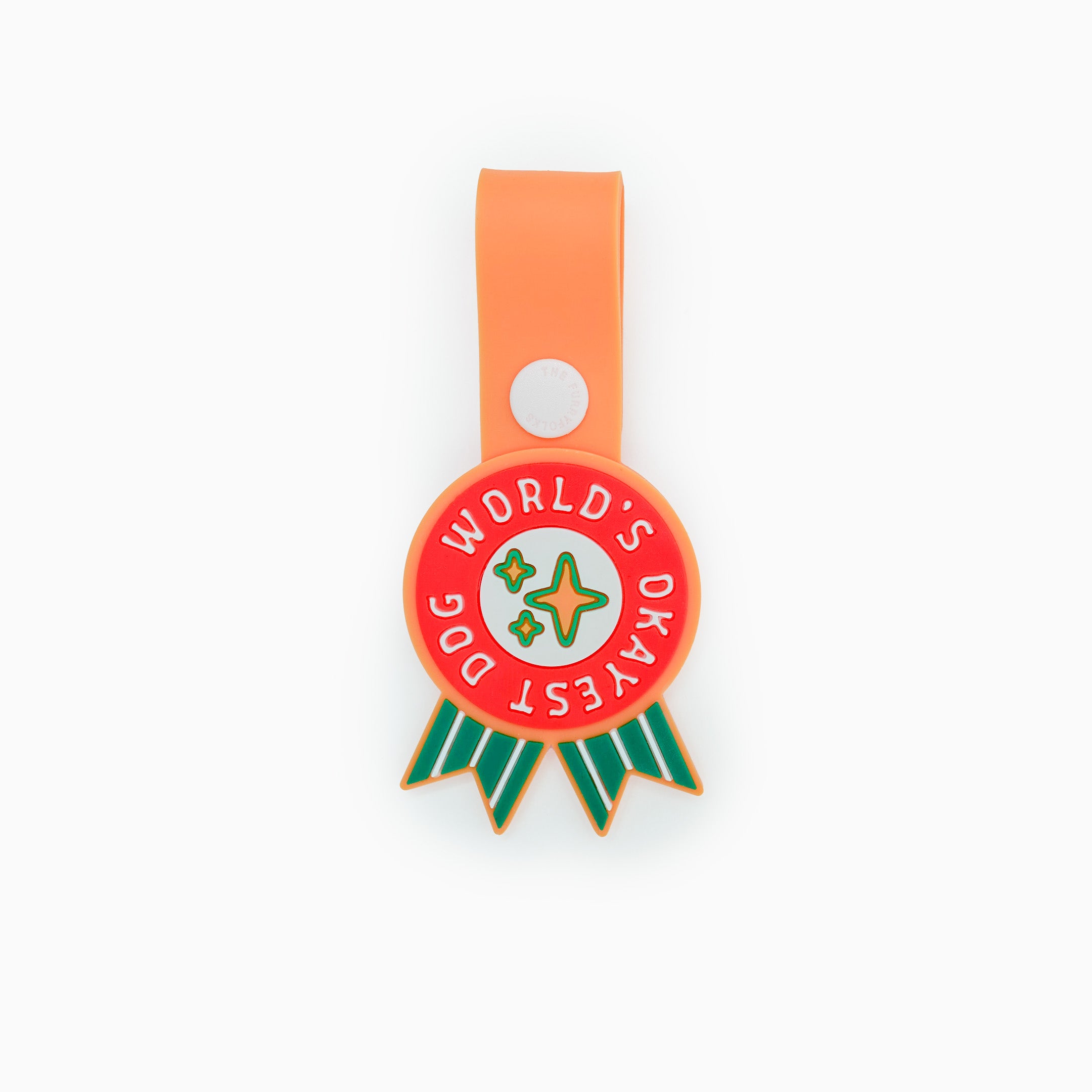 Dog tag with a whimsical design featuring a star and the phrase ‘World’s Okayest Dog’ in bold white text on a red background. The tag has green ribbons at the bottom and is attached to an orange strap with a white button. This playful tag from The Furryfolks’ Daily Clip product line is made from 100% non-toxic rubber and designed to add a touch of humor to your pet’s accessories.