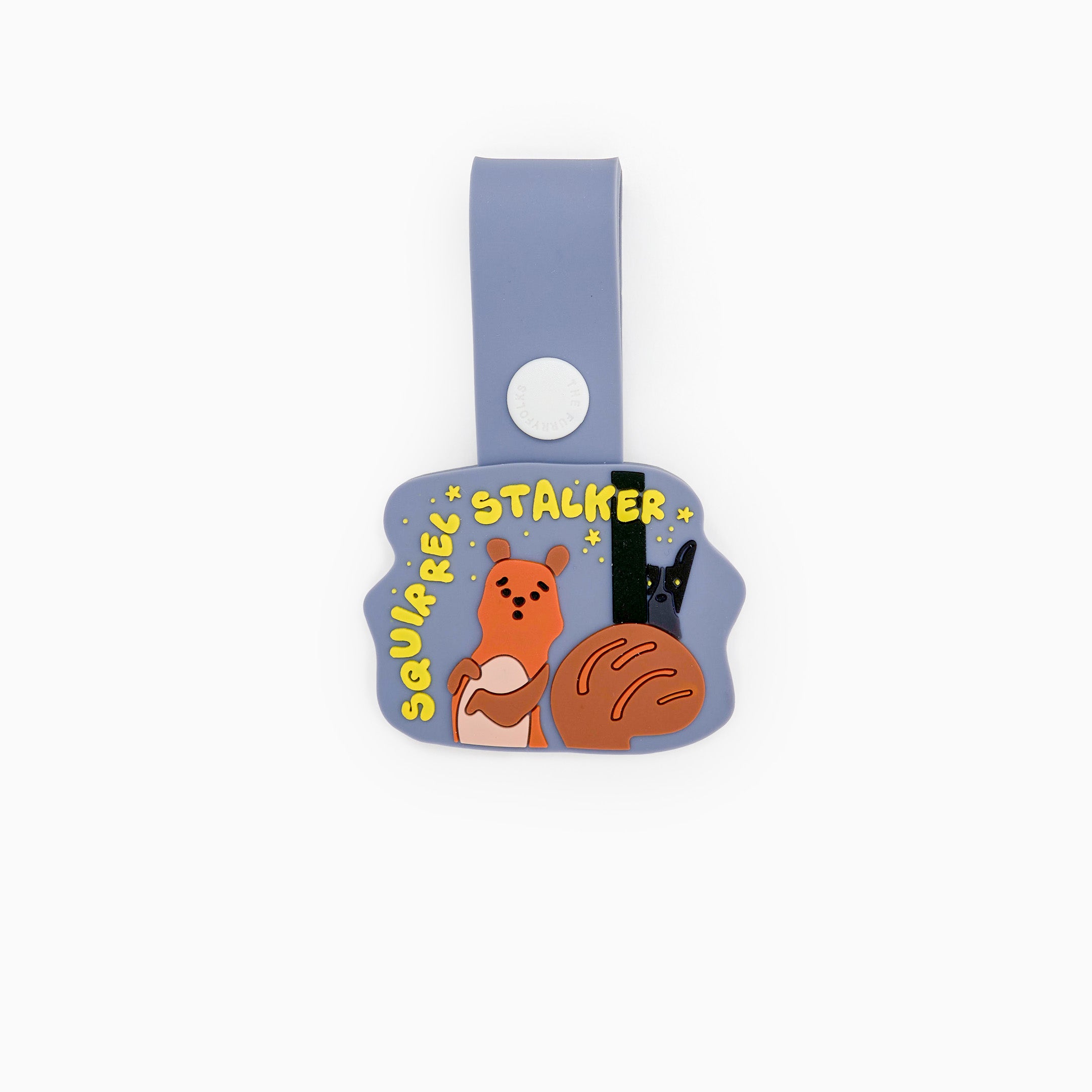 Dog tag with a whimsical illustration of a squirrel and a dog under a starry sky. The tag features the phrase ‘Squirrel Stalker’ in playful yellow text. Attached to a light blue strap with a white button, this charming tag from The Furryfolks’ Daily Clip product line is made from 100% non-toxic rubber and designed to add a touch of humor and charm to your pet’s accessories.