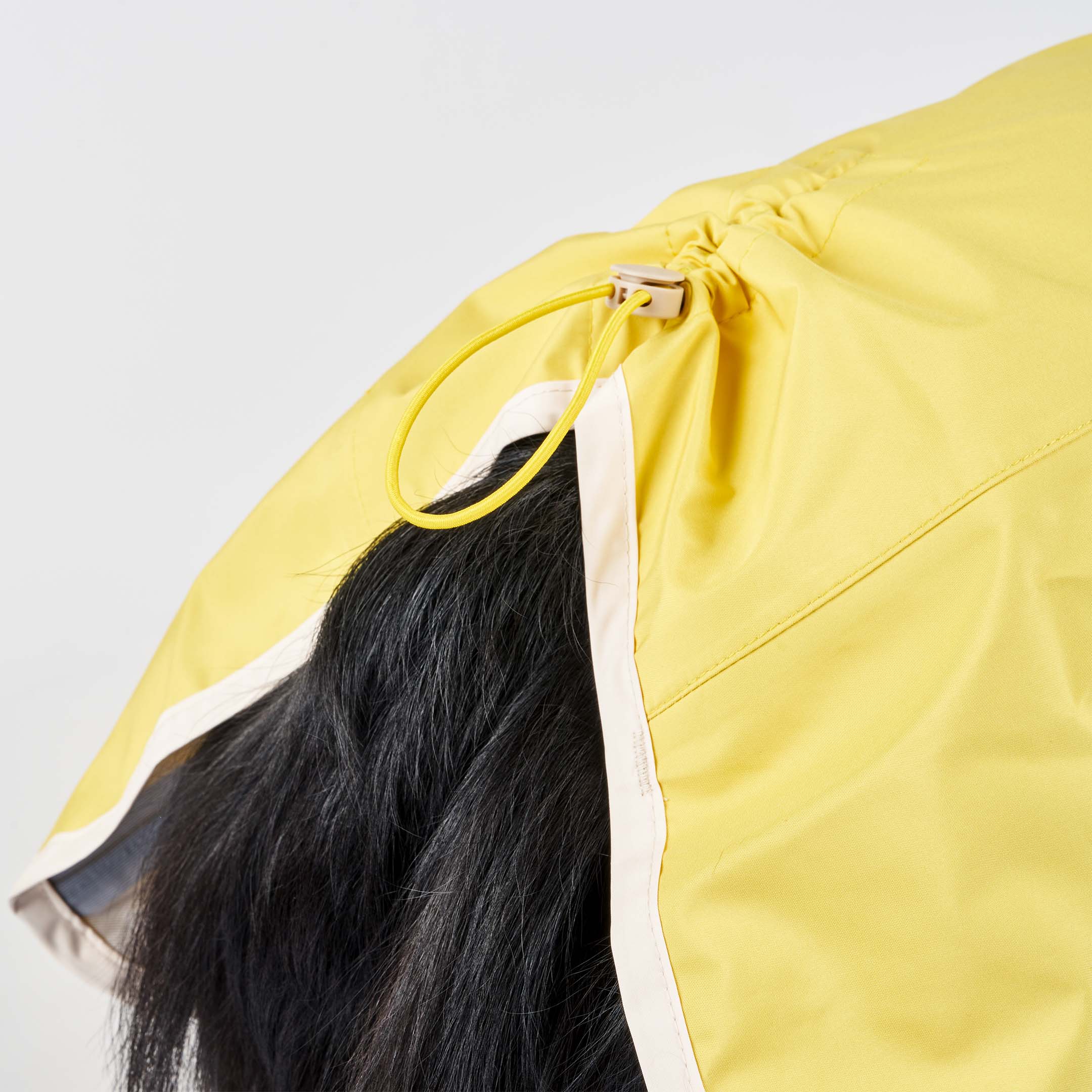 Close-up of a yellow raincoat on a dog, featuring an adjustable drawstring at the back with a loop to secure the fit. The dog’s black fur is visible under the raincoat, showcasing the rain protection design.