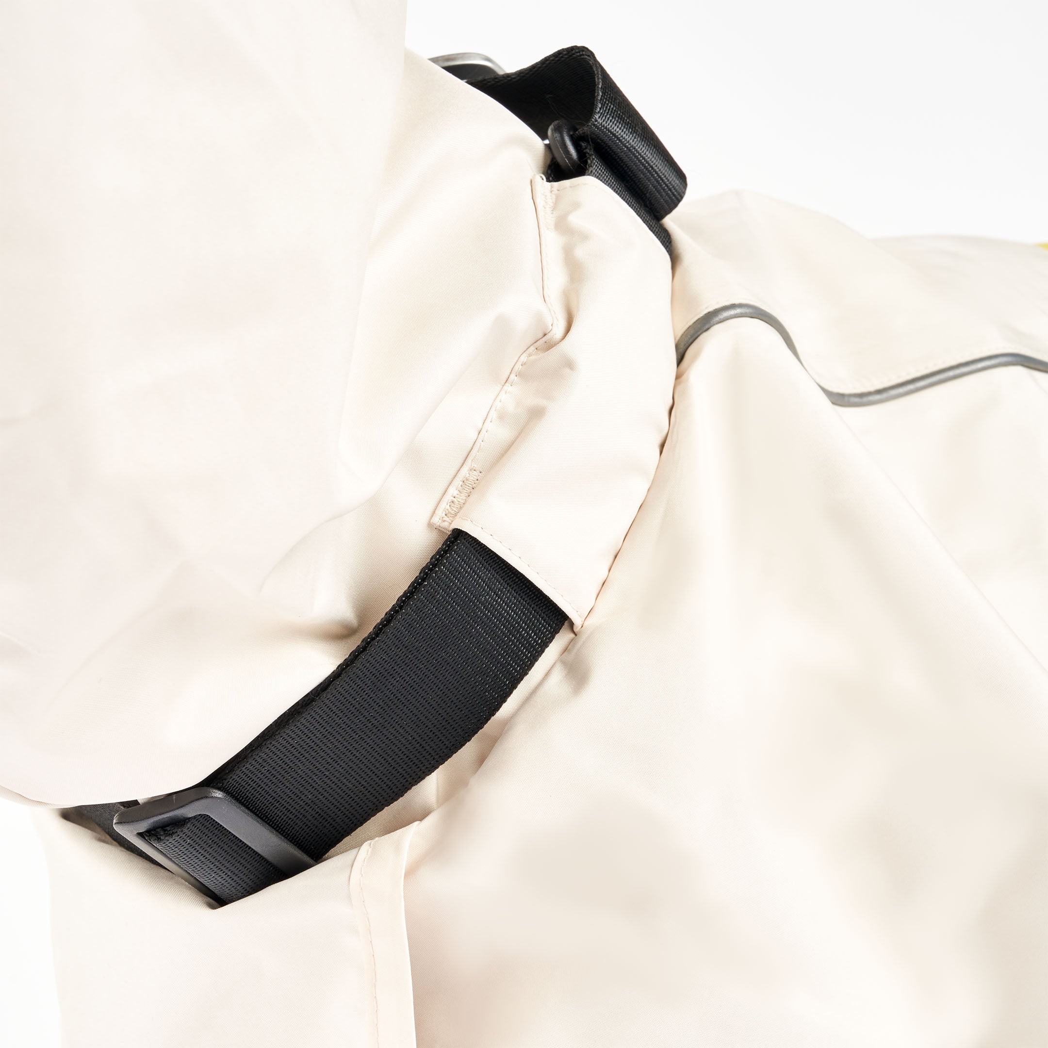 Close-up of a cream raincoat’s neck area on a dog, featuring a black buckle for secure fastening. The raincoat has reflective accents for visibility and a snug fit around the dog’s body.